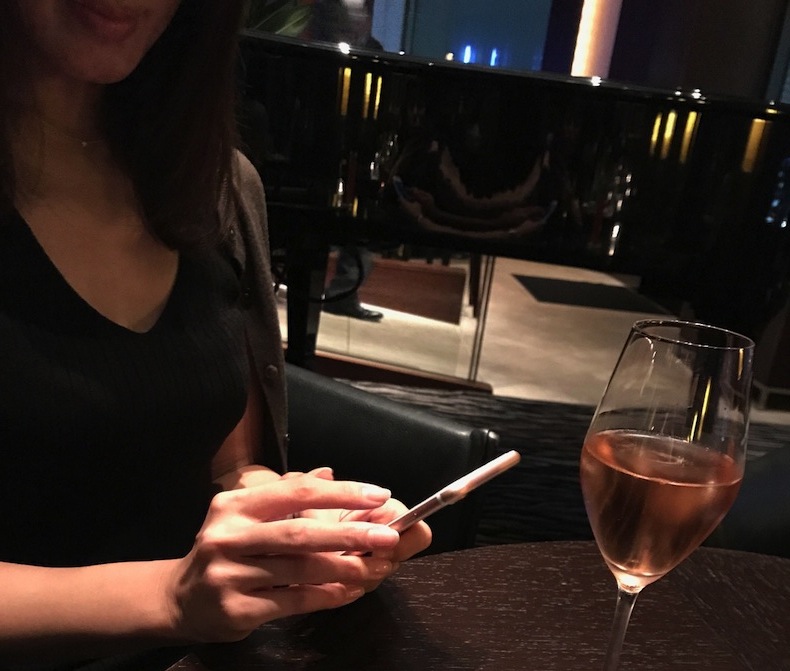 ワイングラスをテーブルに置き、スマホを触る女性