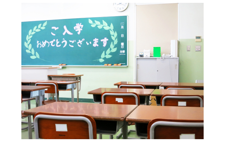 机が並べられ、黒板にはご入学おめでとうございますと書かれている教室の写真