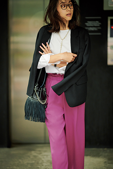 白ブラウスと鮮やかなピンクのパンツに黒ジャケットを肩掛けしたモデル写真