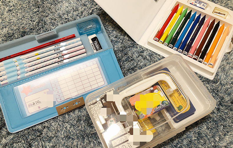 文房具入りの筆箱や色鉛筆、名前スタンプ入りのボックスが置かれている写真