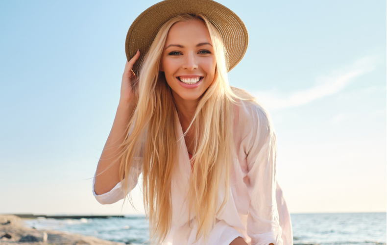 海辺で麦わら帽子をかぶり、笑顔の女性