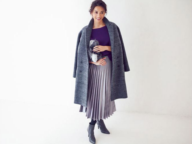 濃い紫のニットとラベンダー色のロングプリーツスカートにグレー地のチェック柄コートを肩がけしたモデル写真
