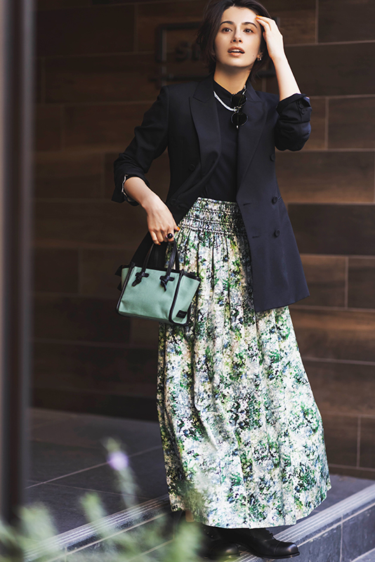 黒カットソーと緑系の花柄のマキシ丈スカートに黒ジャケットをはおったモデル写真