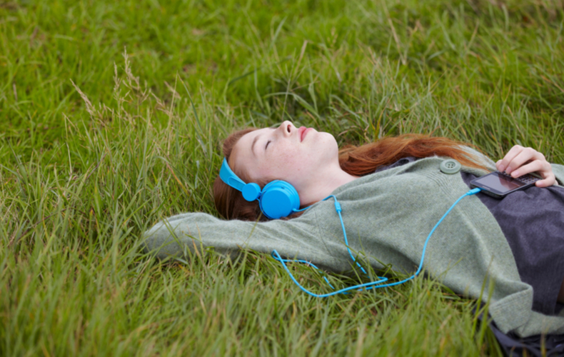 ヘッドフォンで音楽を聴きながら芝生に寝転ぶ人