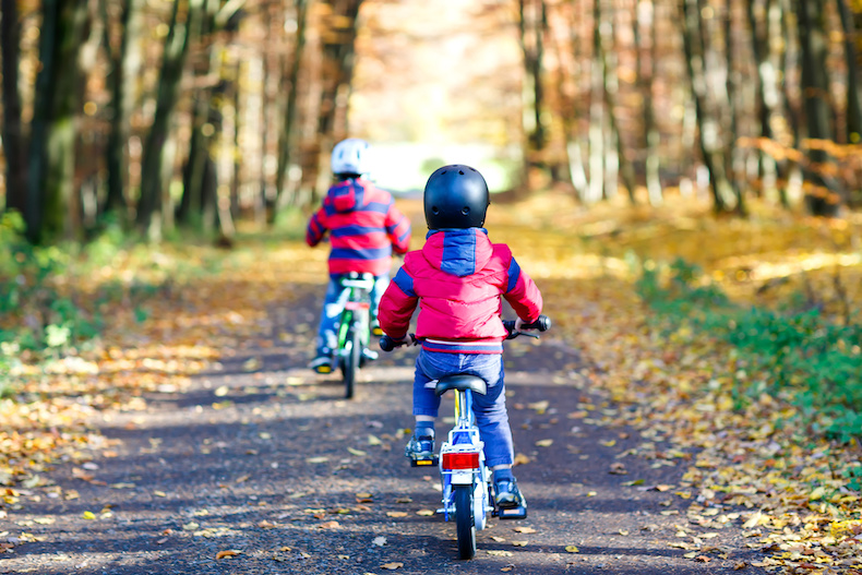 落ち葉の中を自転車で走る2人の子ども