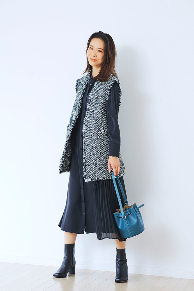 黒のシャツワンピースにツイード素材のジレをはおり、ヒールのあるブーツを履いてブルーのバッグを持ったDomanistの井川加奈子さん