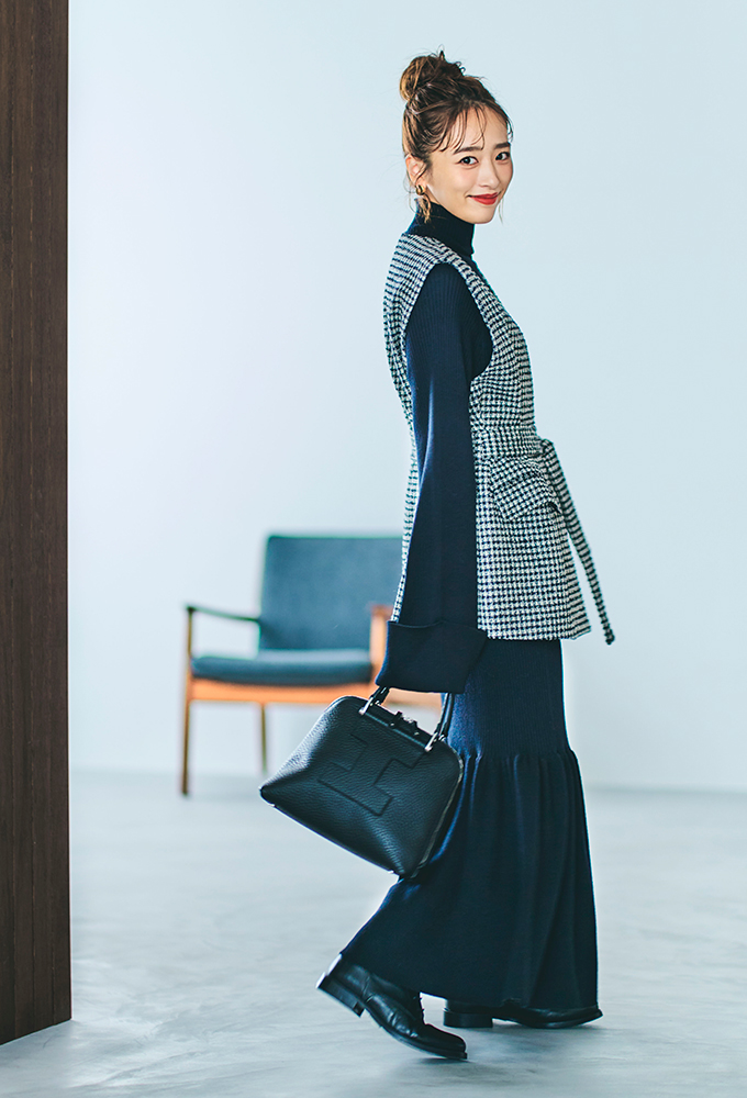 裾がフレアデザインの黒のタートルニットワンピースに白黒のチェック柄のジレを重ね着したモデルの近藤千尋さんの全身写真