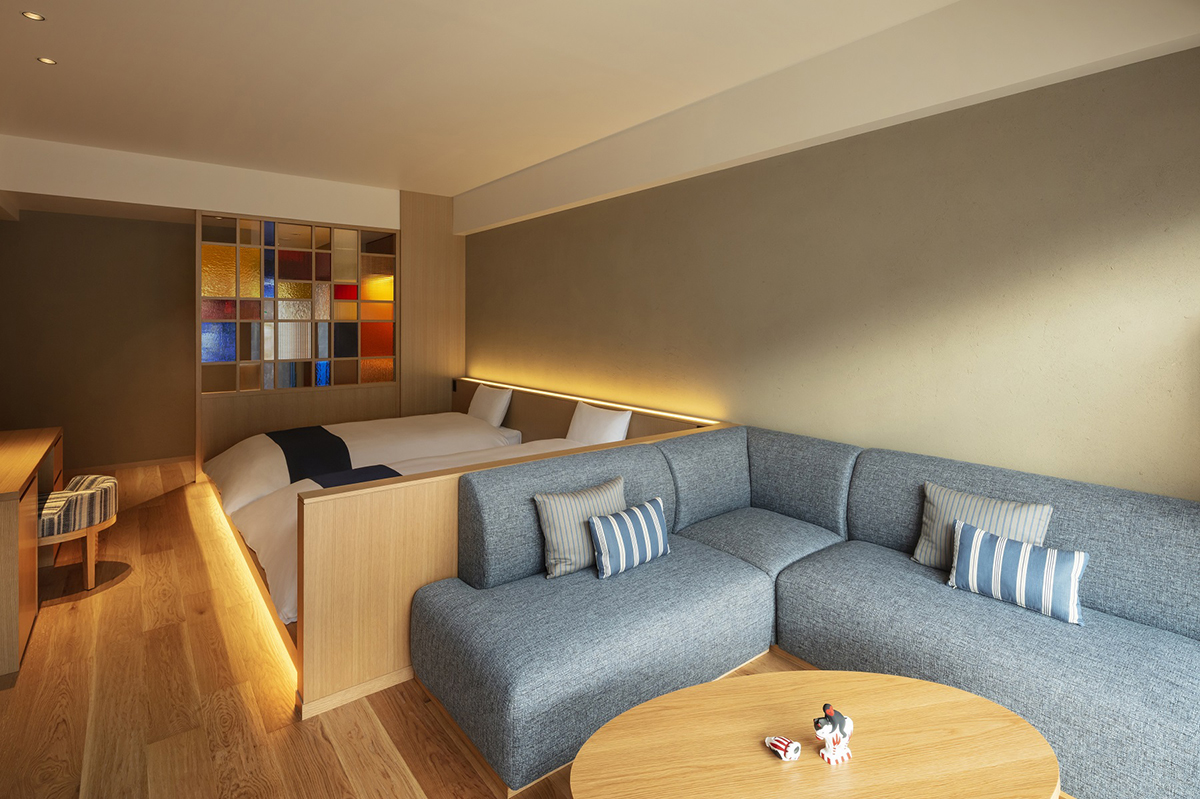 L字型ソファとベッド2台が置かれ、奥にステンドグラスのパーテーションがある客室