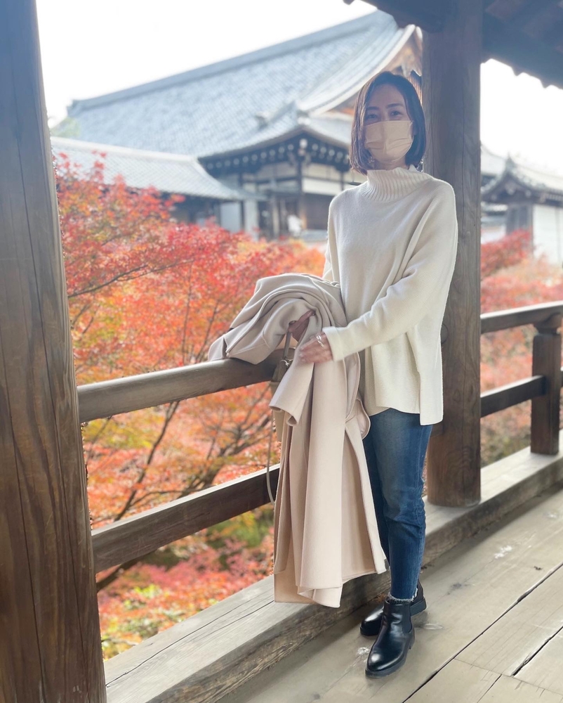 白いニットを着た女性。背景には、東福寺と紅葉が望める景色。