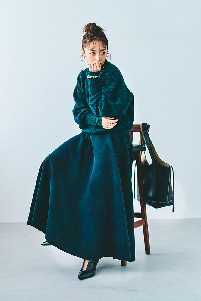 緑のニットとロングスカートを着用し、椅子に座っているモデルの近藤千尋さんの全身ショット