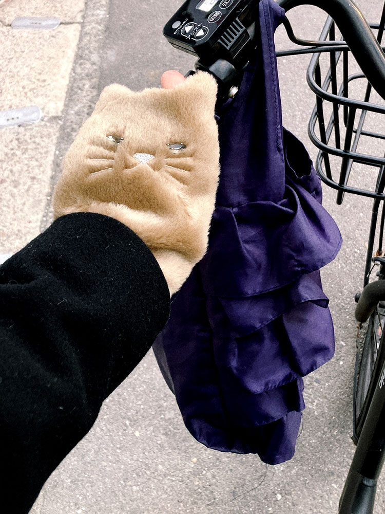 猫をモチーフにした手袋を着用し、自転車のハンドルをにぎる手元