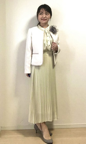 ツヤ感のあるブラウスとスカート、白いジャケットを着用した女性の写真
