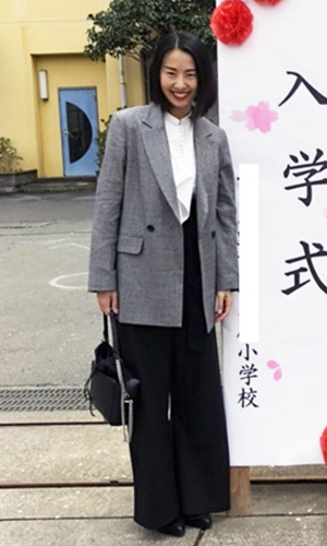 ハイウエストパンツとフリルつきの白ブラウス、グレーのジャケットを着用した女性の写真