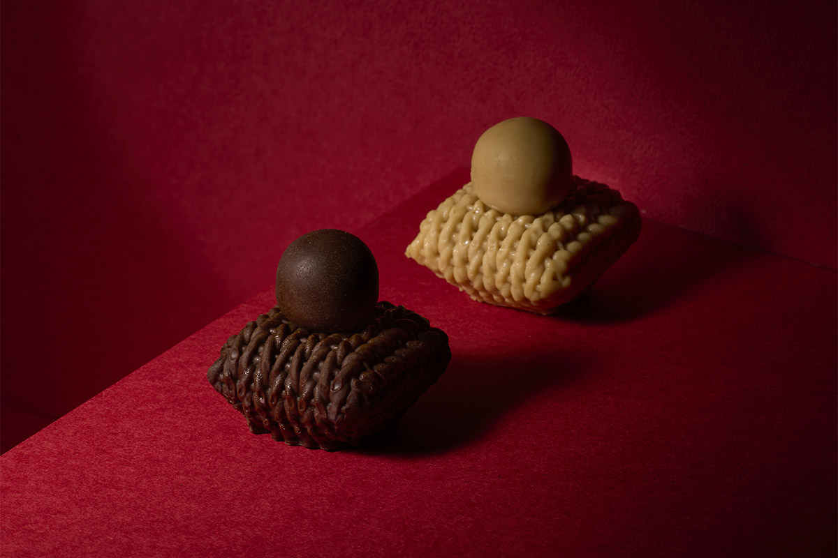 座布団のような形のムースの上に丸いチョコレートが乗った茶色と黄色のお菓子が並んだ写真
