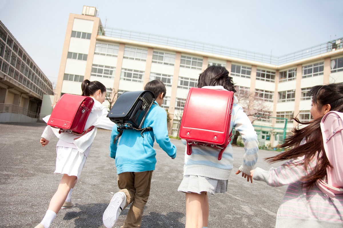 ランドセルを背負って校舎へ走っていく子供たち