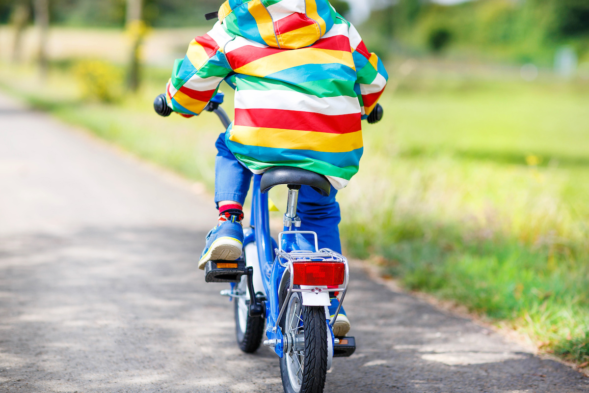 青い自転車に乗ってアスファルト上を走る子ども