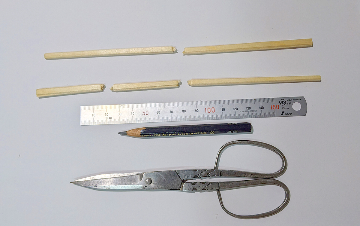 割りばし鉄砲の材料と道具　上から、半分に切った割り箸、半分に切りそのうち1本だけさらに半分に切った割り箸、定規、鉛筆、ハサミ