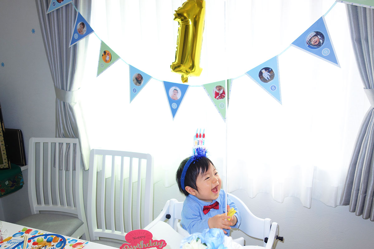 飾りつけした部屋で1歳の誕生日を祝われる幼児