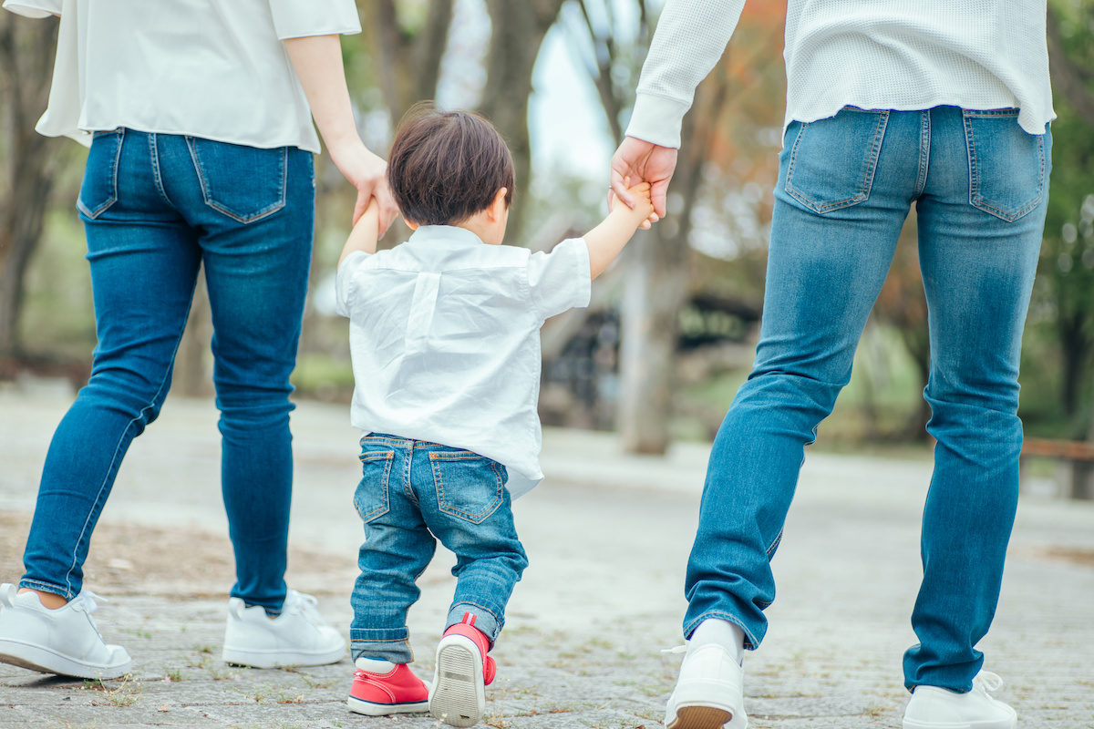 白いトップスにジーンズでお揃いコーデをしている3人家族が手を繋いで歩いている写真