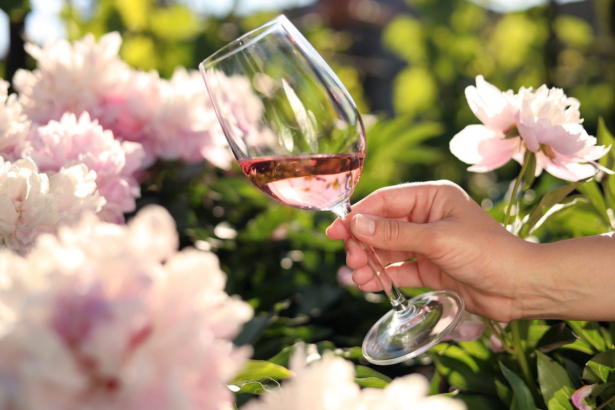 ピンクの花に囲まれたながら、ロゼワインが入ったグラスを持っている手元の写真