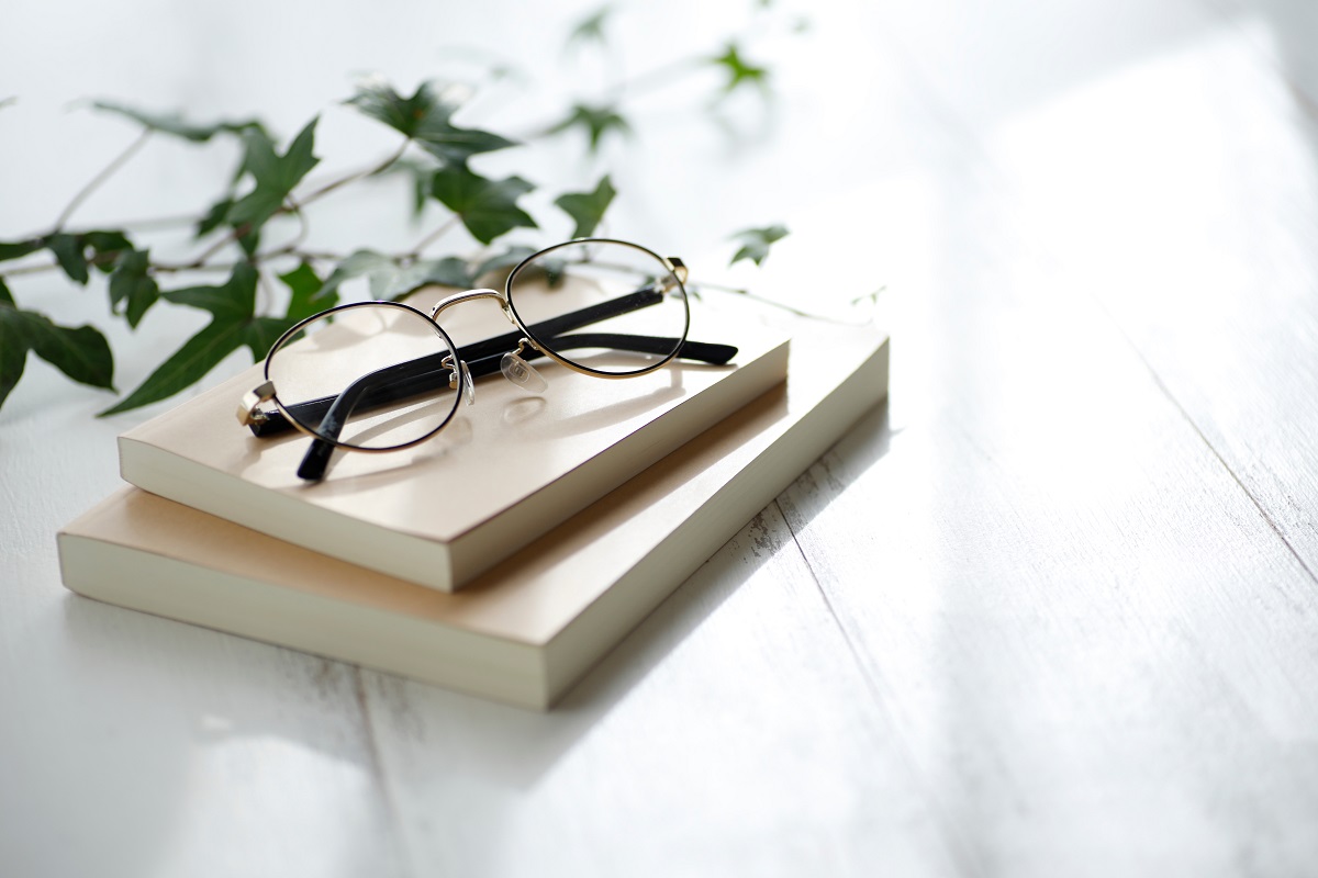 白い木の机の上に置かれた2冊の本とメガネのイメージ写真