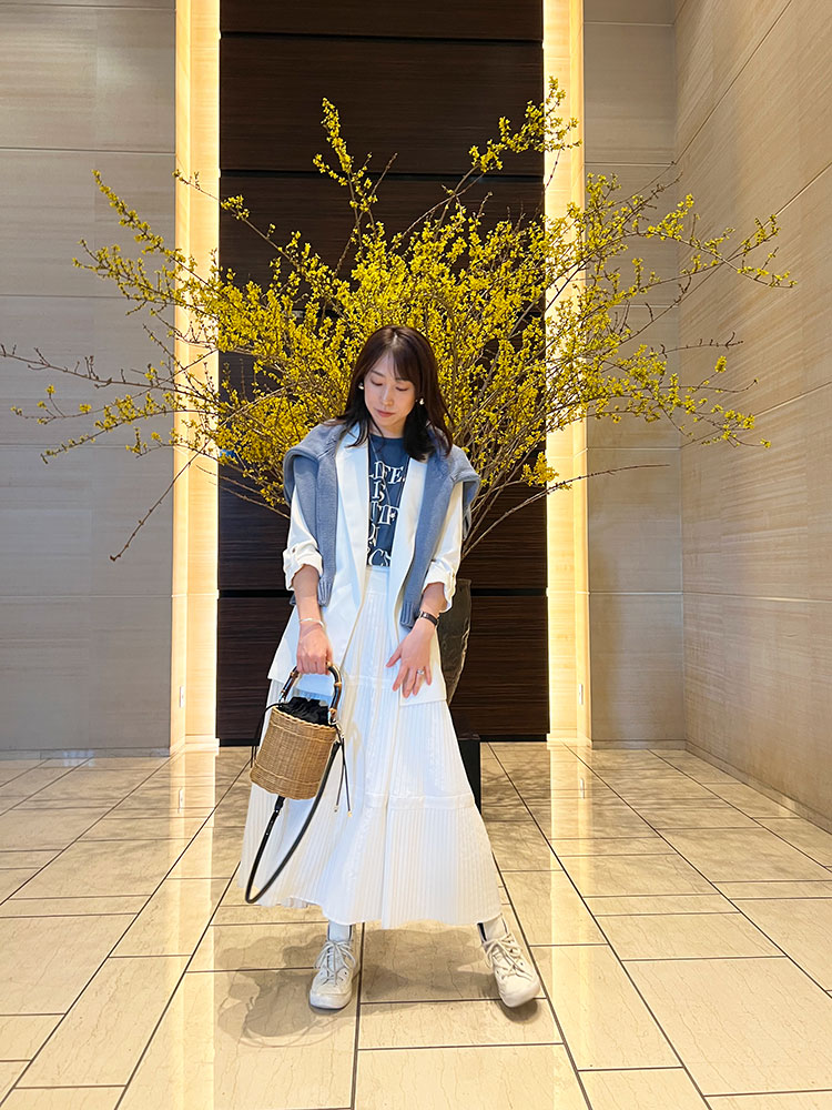 ZARAのカゴバッグを手に持ち、黄色い花の前に立つホワイトコーデの吉田美帆さん