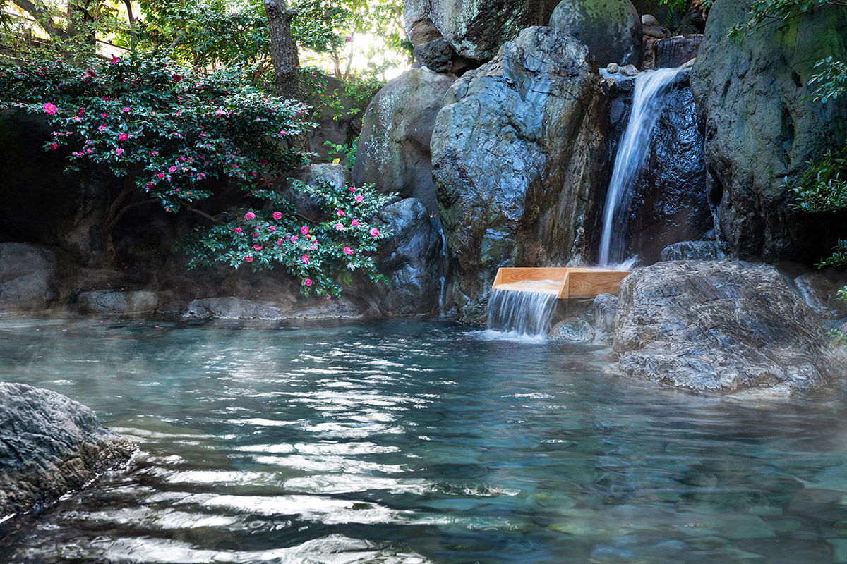 岩で囲まれ、湯の滝が流れ込んでいる露天風呂の写真