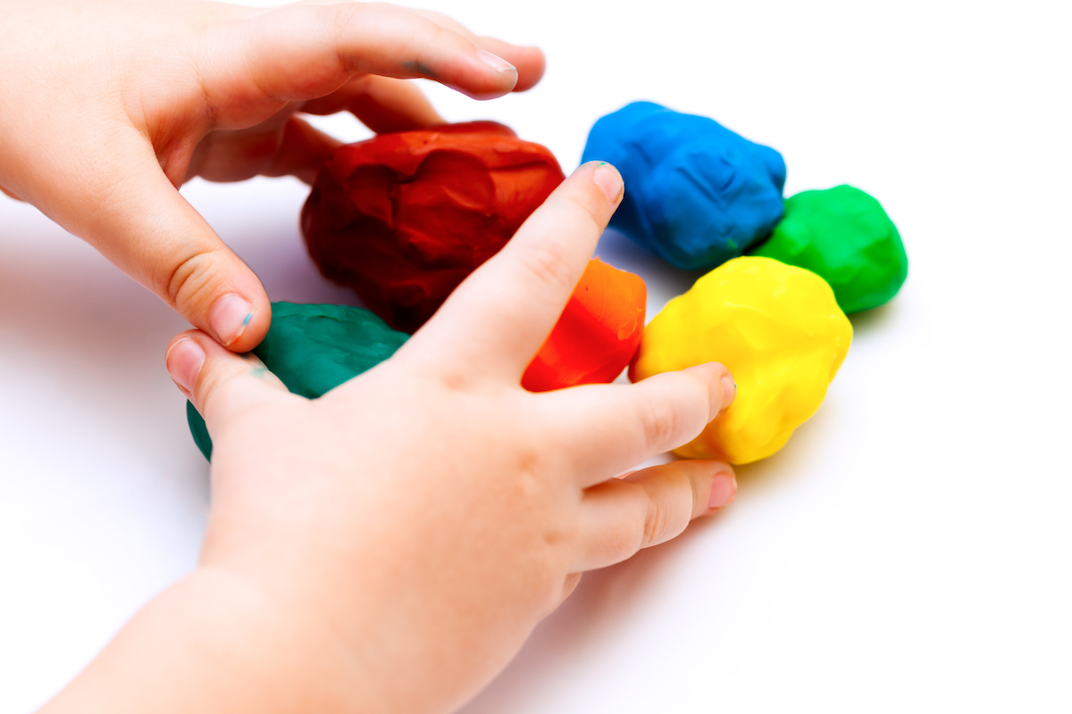 赤やオレンジ、緑、青、黄緑、黄色の粘土を丸めて遊ぶ子供の手元のイメージ写真