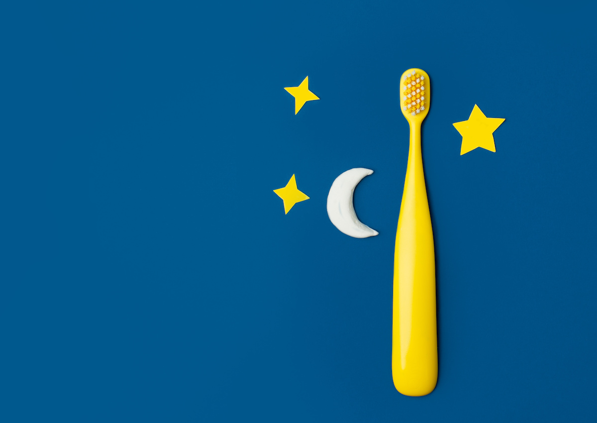深い青の背景に、黄色い子供用歯ブラシと月の形をした歯磨き粉、星の飾りが置かれた写真