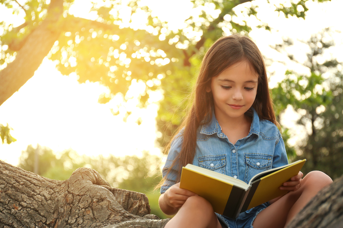木の枝の上で本を広げて読んでいる子供