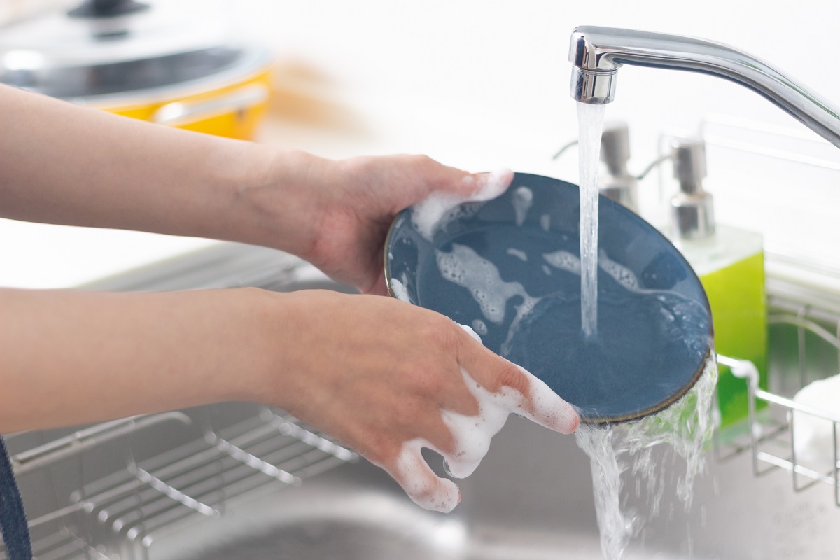 皿洗いのイメージ写真　シンクで食器についた洗剤を流している人の手元