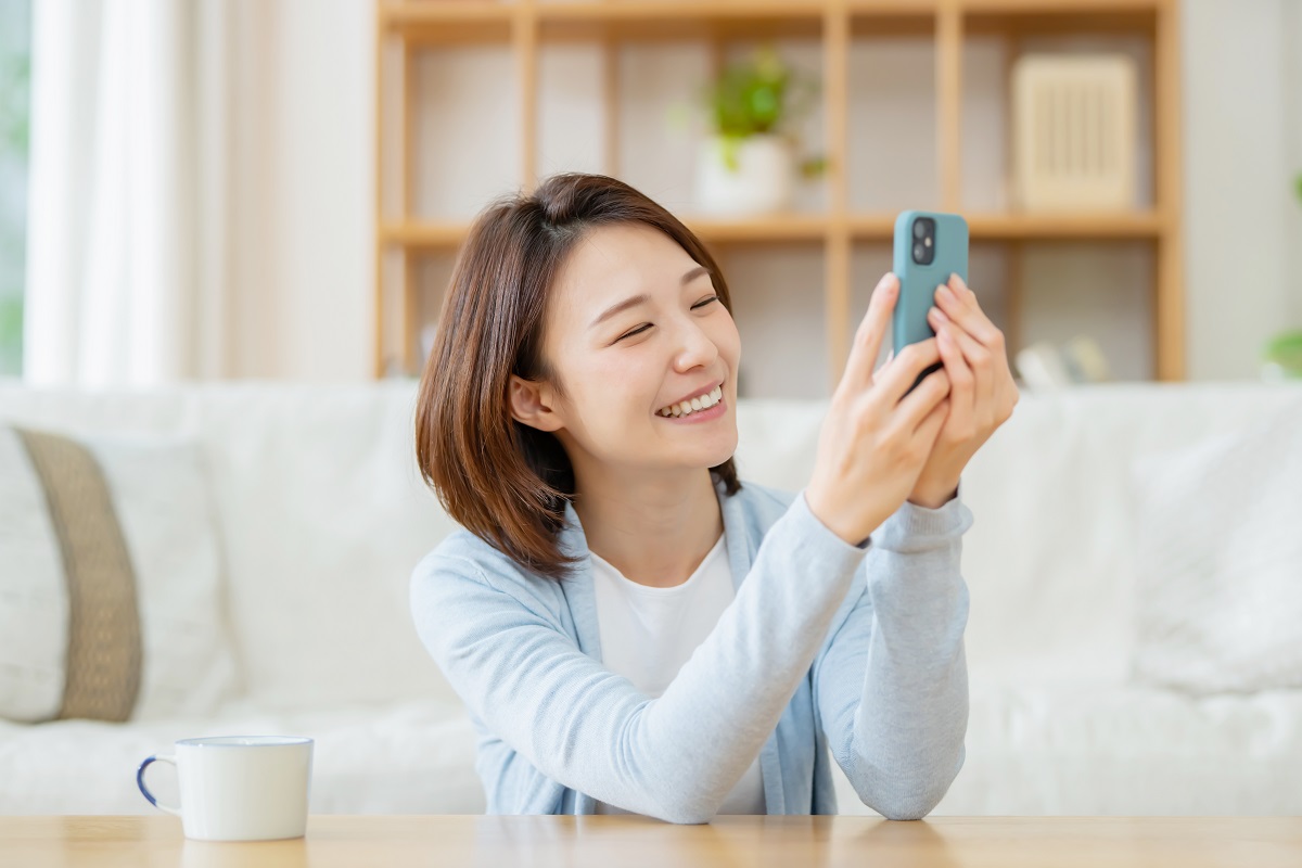スマートフォンを手に持って微笑みながら座っている人のイメージ写真