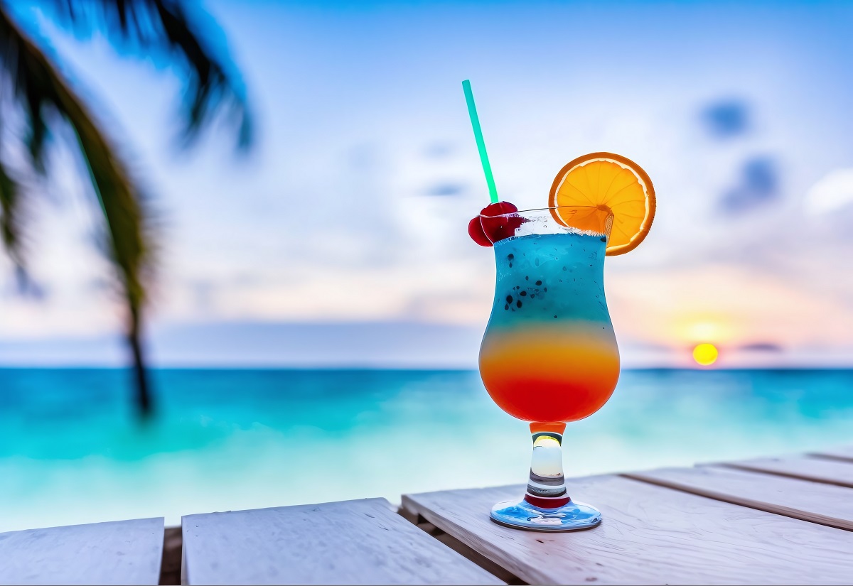 海辺の写真　ウッドデッキの上に、足つきのグラスに注がれた赤と青のグラデーションの飲み物が置かれている