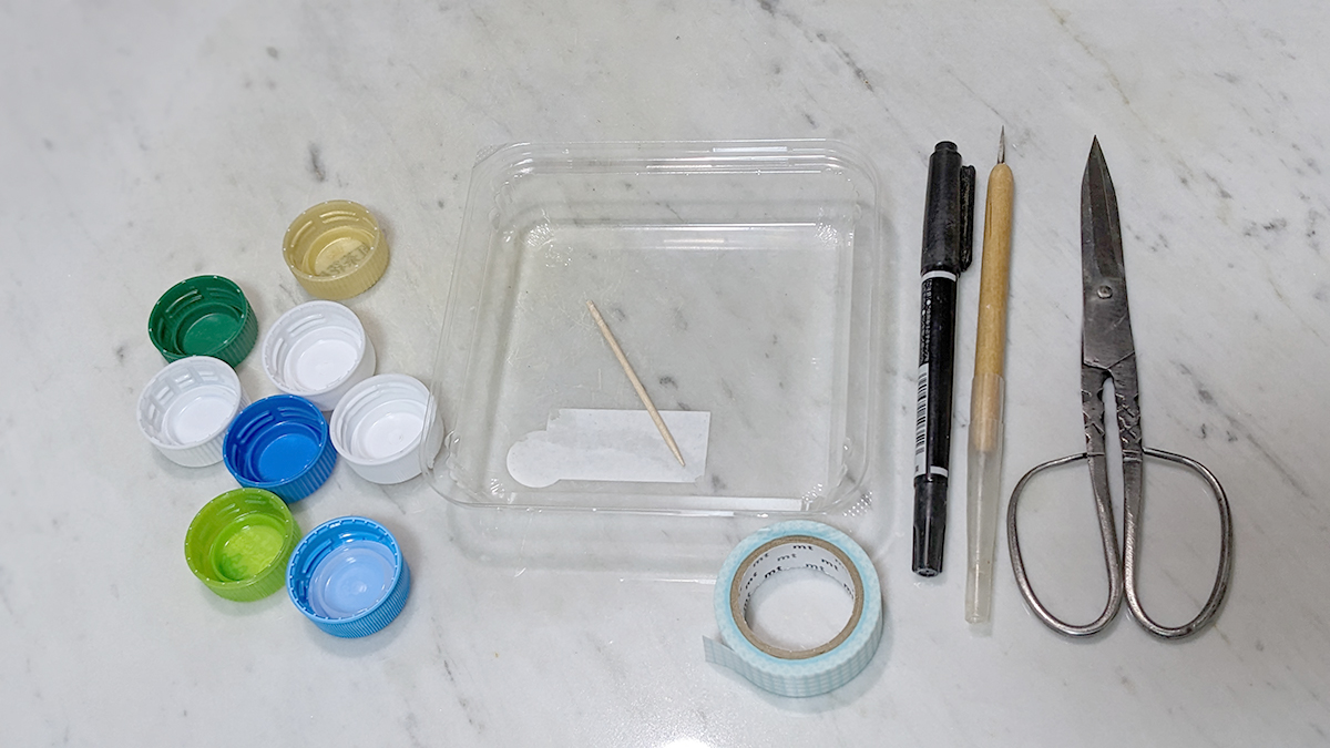 材料の写真　左から ペットボトルの蓋、プラスチックの蓋、つまようじ、マスキングテープ、油性ペン、キリ、はさみ