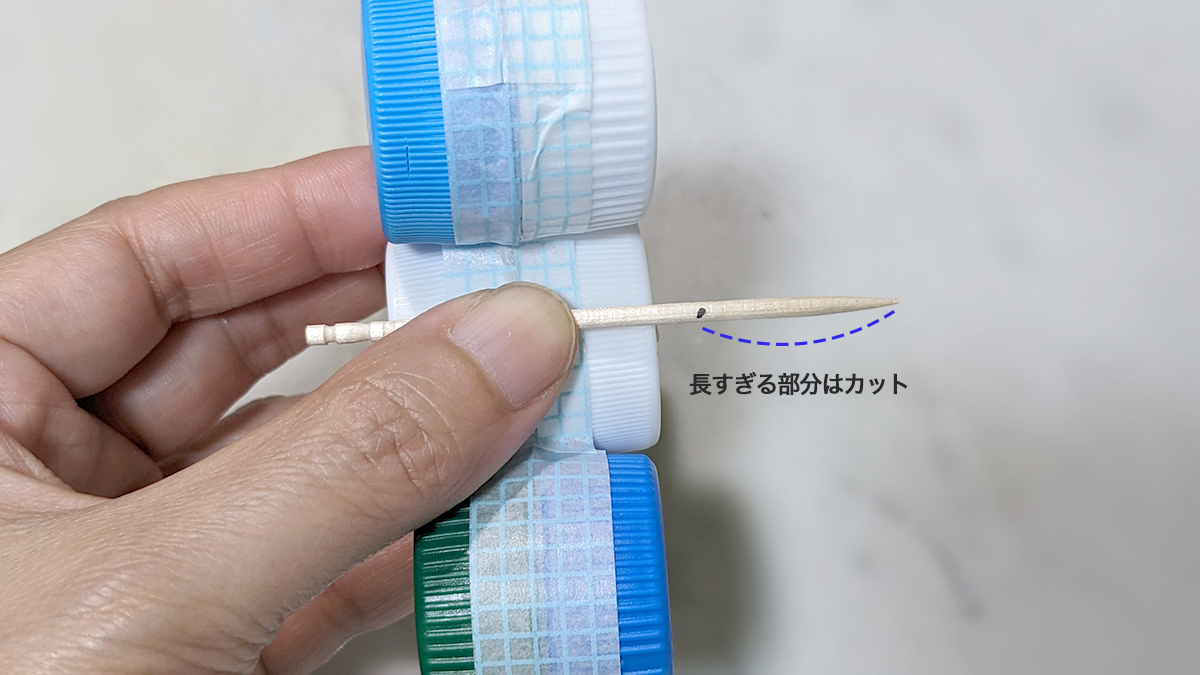 テープで貼り合わせたペットボトルキャップとつまようじを照らし合わせ、サイズをはかっている写真