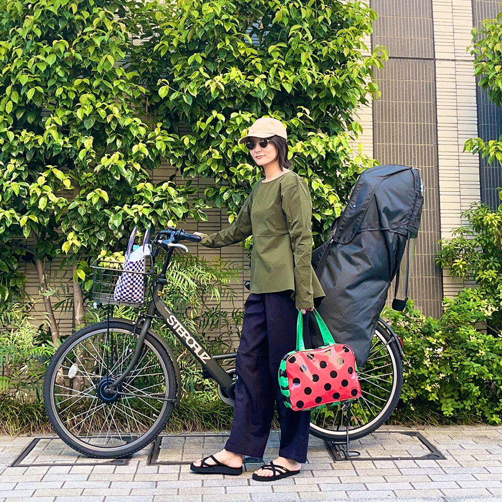 カーキのブラウス風ラッシュガードを着て自転車をおす鈴木まきさん