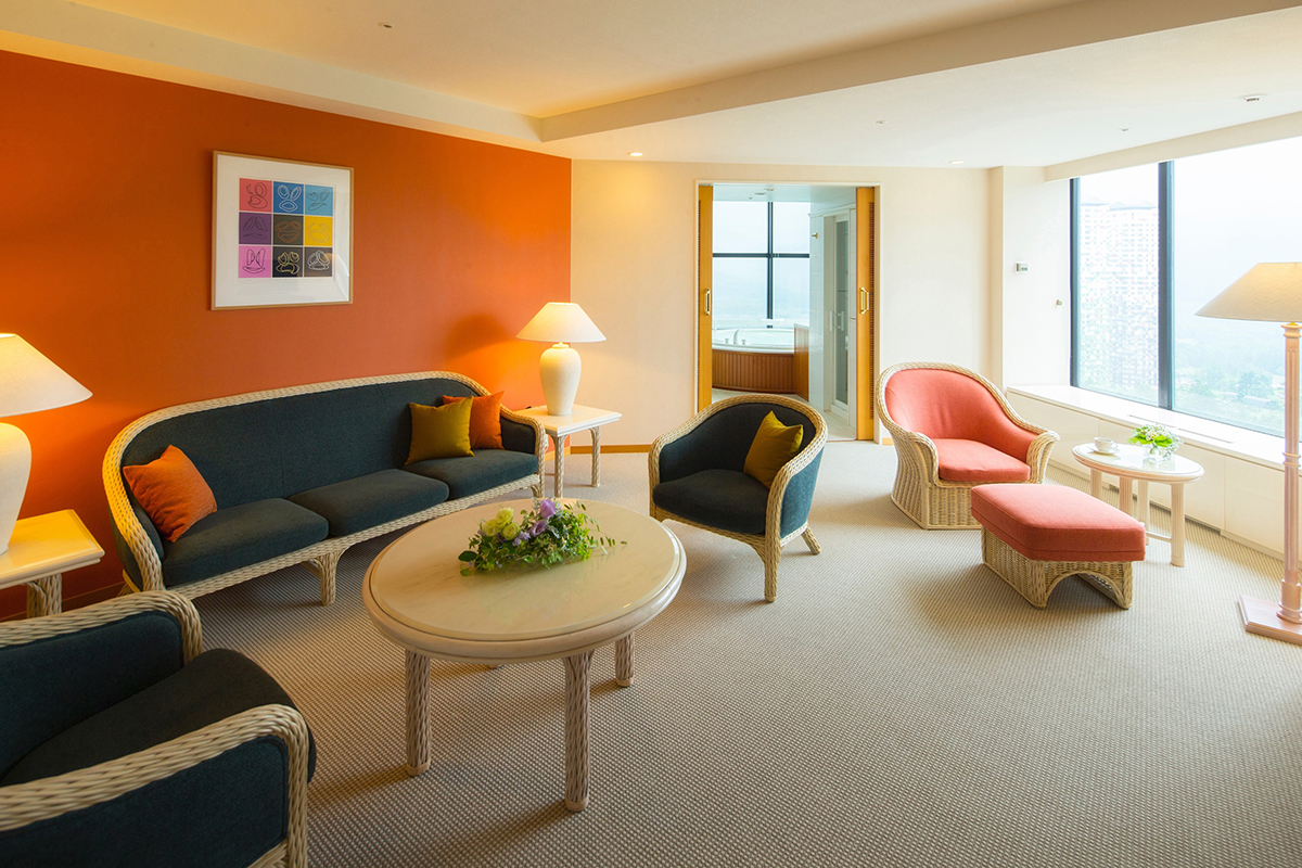 一部の壁がオレンジ色で緑系のソファや暖色のソファが並んだ部屋の写真