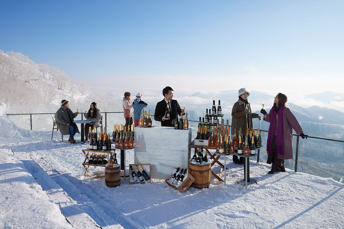 雪景色のテラスに、お酒がたくさん並んだカウンターが設置されており、その周囲では人々が景色を楽しんでいる写真