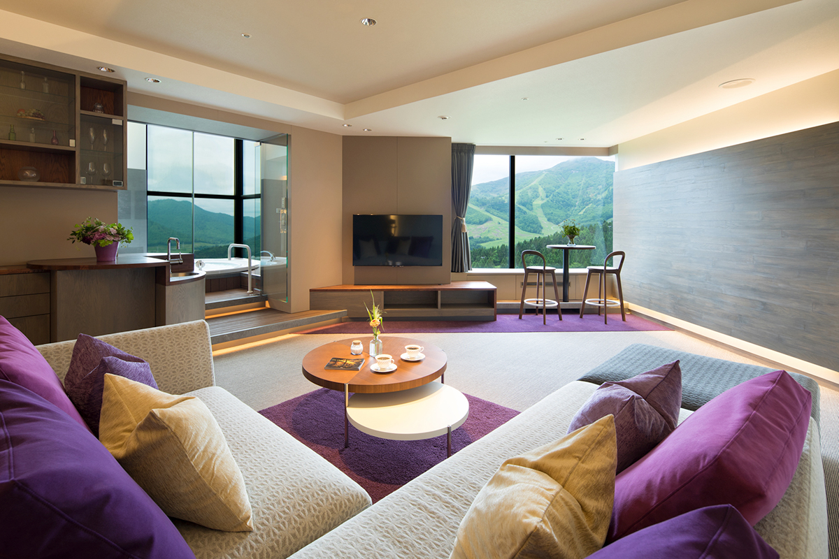テレビやソファ、テーブル、紫色のクッションや絨毯が置かれた部屋の写真