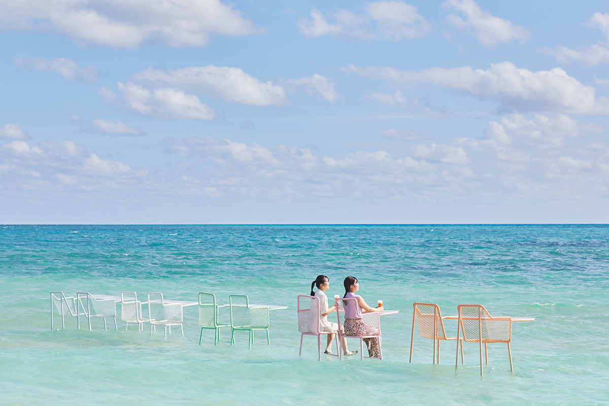 海の上に設置された椅子とテーブルに座る二人組の写真