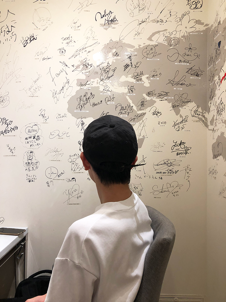 サロンの壁に書かれたたくさんのサインと座っている息子さん