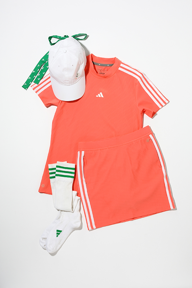 白いキャップ、オレンジの半袖とスカートのセットアップ、白と緑のソックス