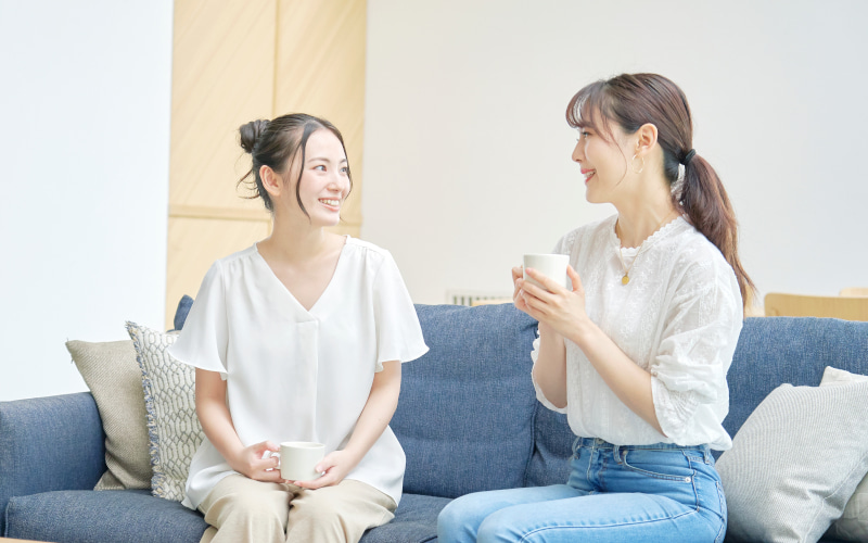家の中でマグカップを片手におしゃべりをする二人の女性