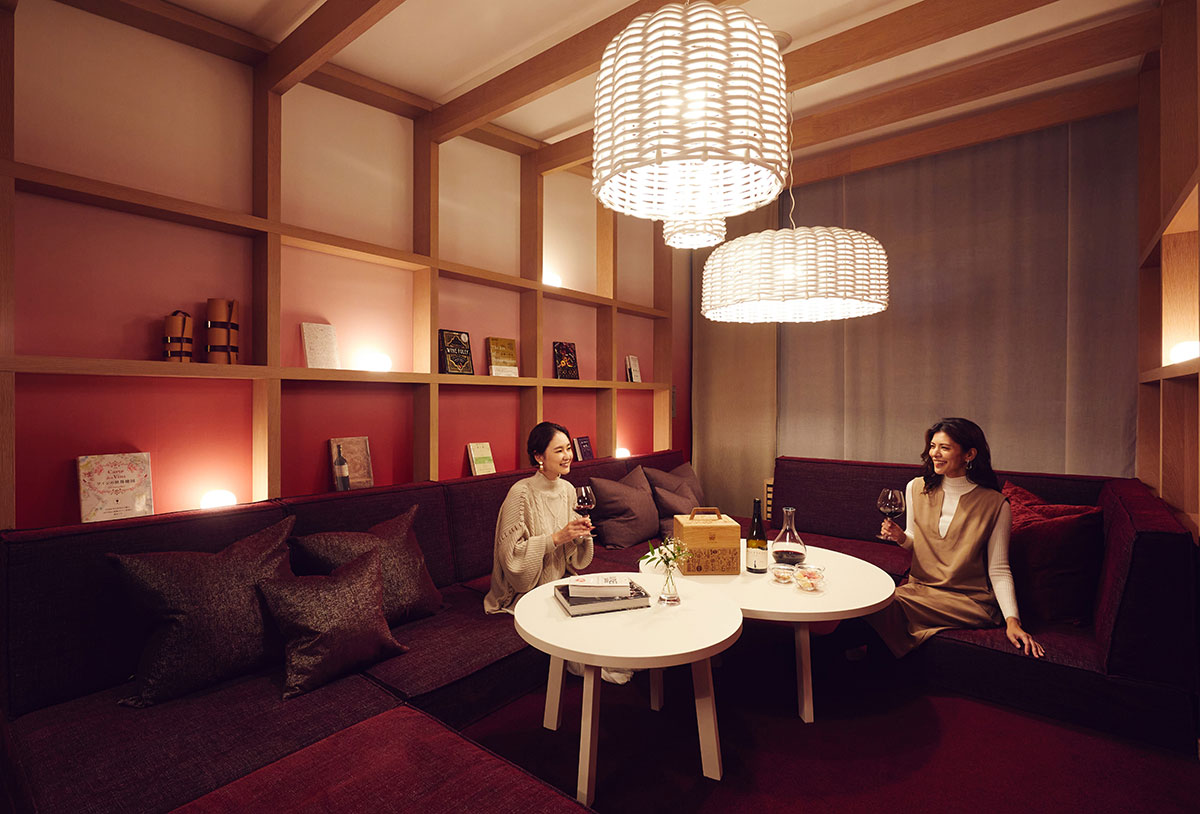 格子状の飾り棚のある部屋でワインを飲みながらソファに座る二人の写真