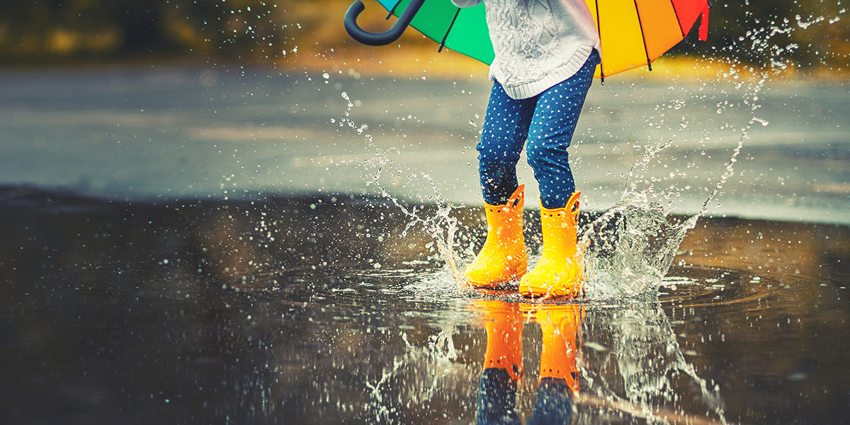 傘をさし、長靴で水たまりに踏み込む子ども