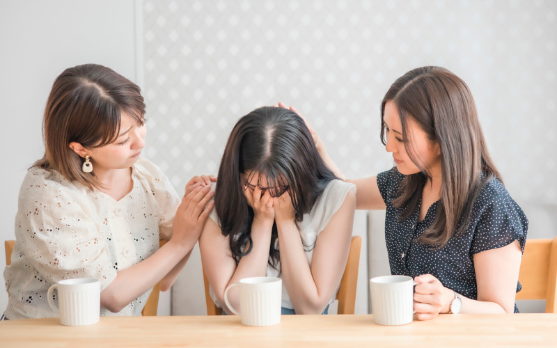 女性三人の写真。真ん中の友人が泣いており、両脇の二人が慰めている