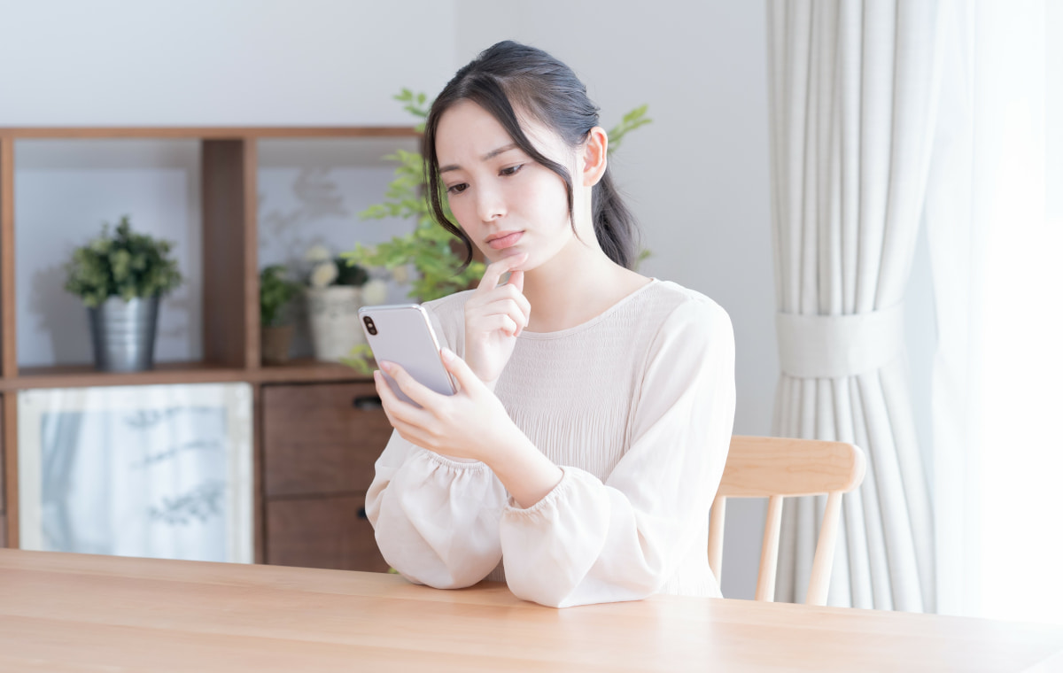 スマホを見ながら悩む女性の写真