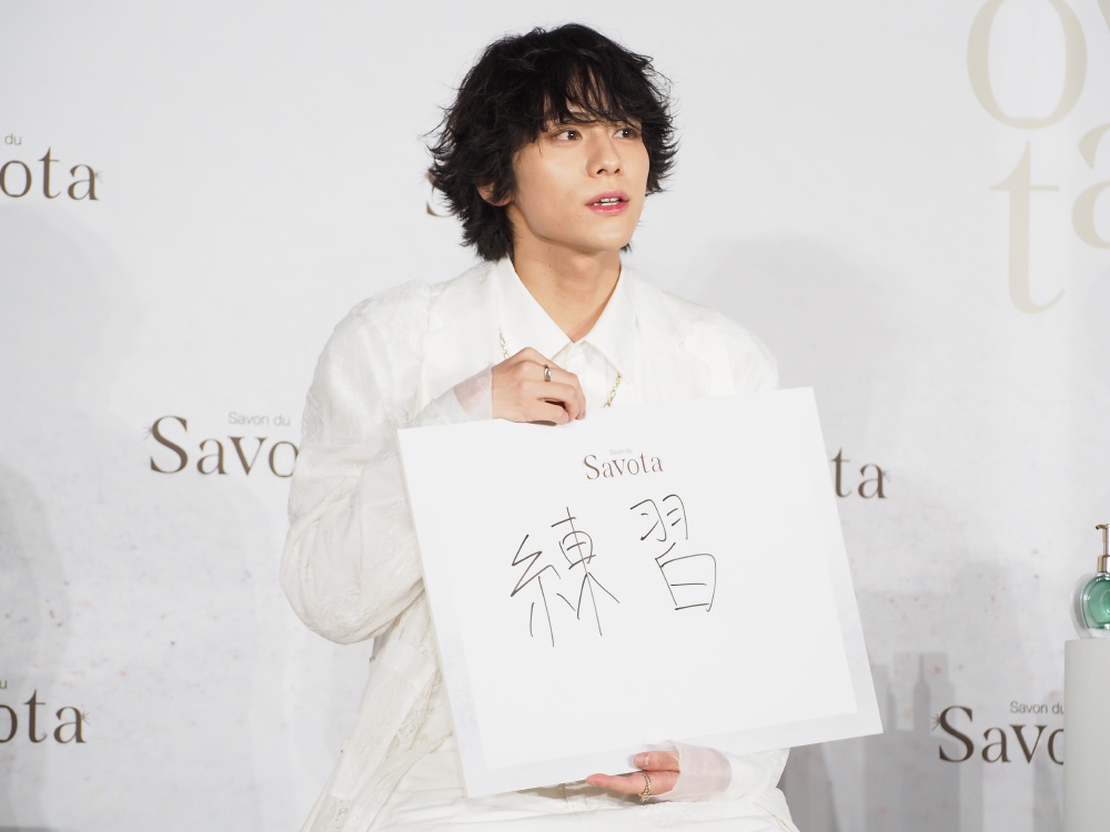 「練習」と書かれたフリップを持つ山下さん