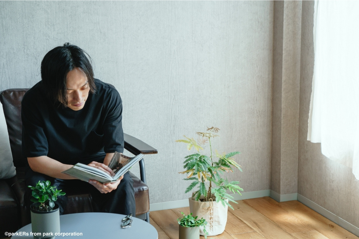 植物のある部屋で本を読む男性