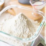 ガラス容器に入った小麦粉の写真。はかりで重さをはかっている